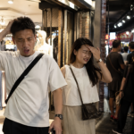 夜市逛街時，一對情侶從冷氣充足的服飾店走到戶外，瞬間感受到炎熱天氣帶來的強烈溫度落差。畫面以寫實攝影風格呈現夜市人潮、服飾店與夏日悶熱氛圍，呼應文章探討「人的感受是相對值」、「基準如何形成」、「適應力」、「社會比較」以及「經驗如何塑造認知基準」等心理學觀點。